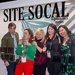 Five people stand together smiling in front of a glass wall with "SITE SOCAL" written on it, appearing to pose for a group photo at an event.