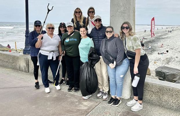 A group of six people smiling and holding trash bags on a sunny beach during SITE SoCal Young Leaders’ Annual Beach Cleanup.