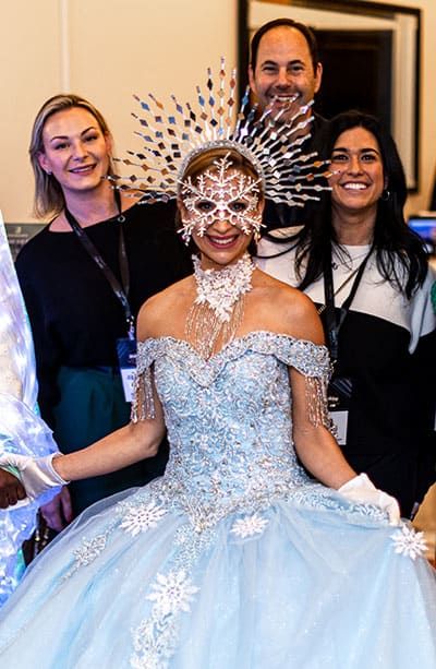 Three people pose and smile at SITE SoCal Holiday Event; a man in a patterned suit stands in the middle with two women in dresses on either side, each holding a drink.